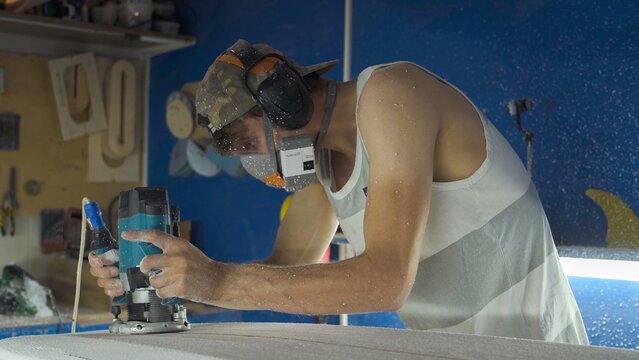 Male surfboard shaper making surfboard in his workshop. Hand shaping from blank.