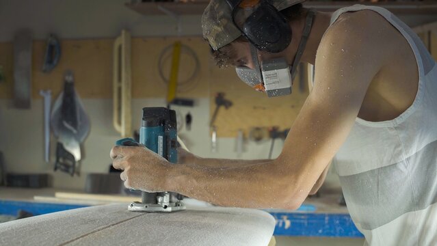 Male surfboard shaper making surfboard in his workshop. Hand shaping from blank.