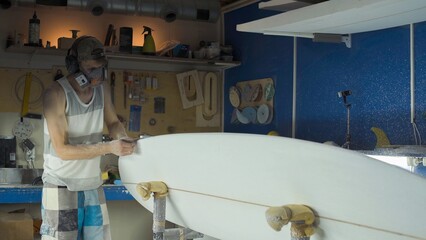 Male surfboard shaper making surfboard in his workshop. Hand shaping from blank.