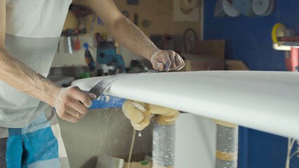 Male surfboard shaper making surfboard in his workshop. Hand shaping from blank.