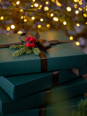 Christmas gifts in green boxes with brown bow near the tree with bokeh Christmas lights in...