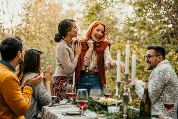 The joyous ambiance of a garden party, with a lesbian proposal with a diverse group of people relishing a shared meal amidst nature's beauty.