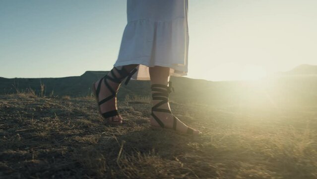women's legs feet close-up walk along beach river banks, stepping barefoot on yellow sand. Woman enjoys summer nature free life water green tree sun light. Girl walks go in white long old style dress
