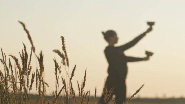 Slowmo of couple of professional artists rehearsing for extreme fire show performance in field at sunset with wheat fluttering in wind in focused background