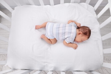 Cute newborn baby sleeping in crib at home, top view. Bedtime