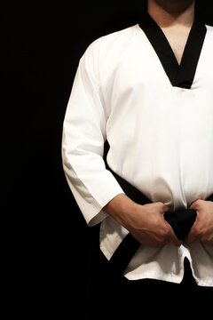 Deportista fuerte masculino con dobok blanco, cintur&oacute;n negro de medio cuerpo en un fondo negro