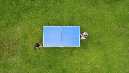 Aerial view people playing ping pong match outdoor. Top view two boys playing table tennis on a green grass lawn. Aerial view outdoor sport