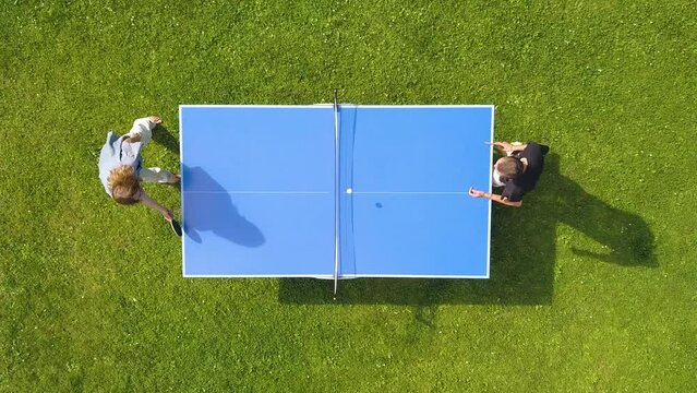 Aerial view people playing ping pong match outdoor. Top view two boys playing table tennis on a green grass lawn. Aerial view outdoor sport