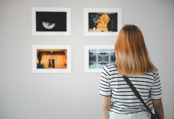 Asian young woman standing she looking art gallery in front of colorful framed paintings pictures...