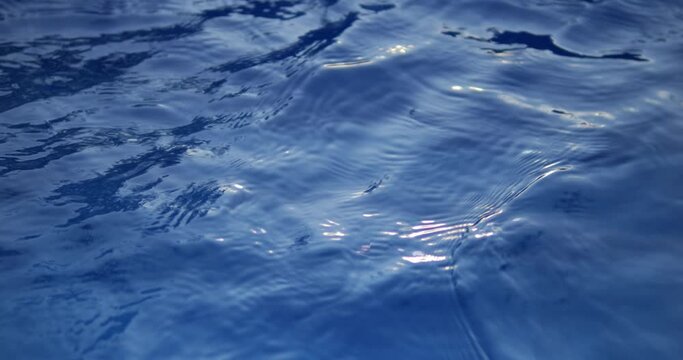 Water surface with gentle waves on a blue background. Deep waters of the blue ocean. Splashing water in the pool.