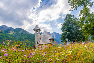 The beautiful Catholic Church in the valley of Theth national park with pink summer flowers, Albania. albanian alps