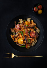 Fusilli pasta with mushrooms, asparagus and cherry tomatoes on a modern design plate with dark background