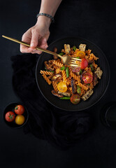 Fusilli pasta with mushrooms, asparagus and cherry tomatoes on a modern design plate with dark background