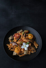Fusilli pasta with mushrooms, asparagus and cherry tomatoes on a modern design plate with dark background