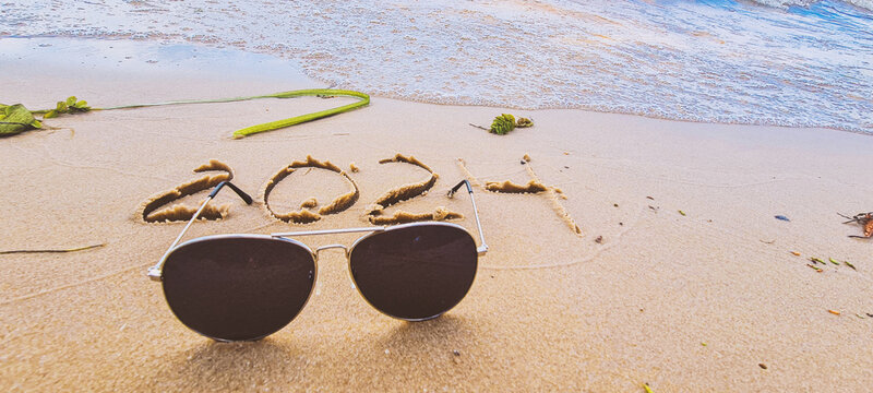 The inscription 2024 on the wet sand on the beach. Nearby are sunglasses