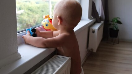One year old baby boy playing with toys standing near the window on the windowsill at home