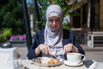 Caucasian woman in hijab having breakfast in outdoor cafe. 