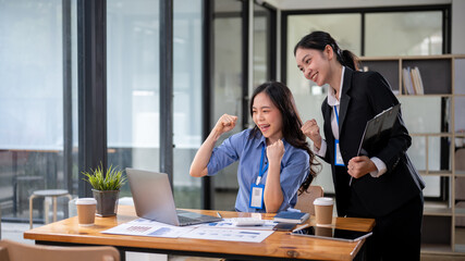 Two cheerful Asian businesswomen are looking at a laptop screen with a happy face