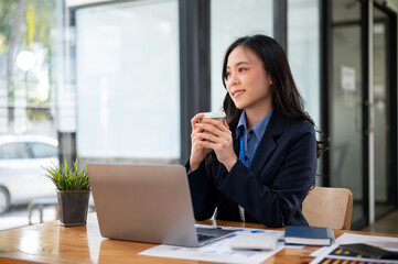 Obraz premium A beautiful Asian businesswoman is looking out the window and daydreaming about her career success.