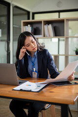 A thoughtful and focused Asian businesswoman is reading documents at her desk in the office.