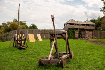 An old siege catapult and a wooden defensive structure in the background, mockups, summer day.