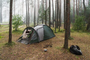 Wild camping in the forest, a tent in nature during the rain, a husky dog ​​sleeps nearby.