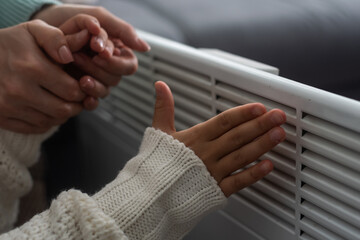 Family warming hands near electric heater at home, closeup