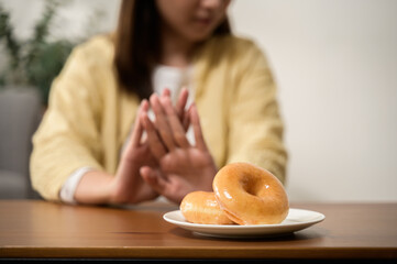 Dieting or good health concept. Young woman rejecting junk food or unhealthy food such donut because concern about health sickness and body weight. Young woman self care food control diet concept. - obrazy, fototapety, plakaty