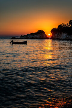Sunset over the sea. The sun is setting between two rocks in the horizon, with a small motor boat anchored near by
