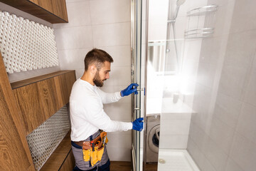 Young plumber fixing shower cabin