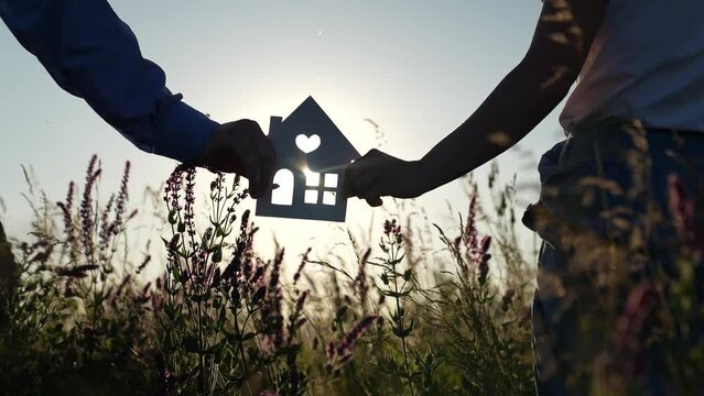 symbol sign silhouette house sunset. the light of the sun shines through the window. housewarming house construction. family hands holding paper house at sunset. dream buying house. construction