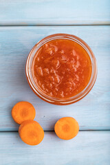 Carrot jam with cinnamon in glass jar on blue wooden. Top view.