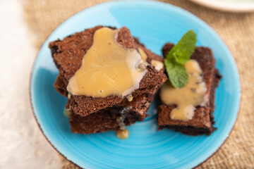 Chocolate brownie with caramel sauce with a cup of coffee on gray concrete, side view, selective focus.