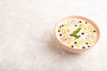 Yoghurt with bilberry and caramel in ceramic bowl on gray concrete, side view, copy space.