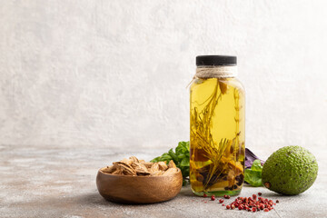 Sunflower oil in a glass jar with various herbs and spices on a brown concrete. Side view, copy space.