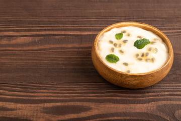 Yoghurt with granadilla and mint in wooden bowl on brown wooden, side view, copy space.