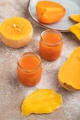 Baby puree with pumpkin, persimmon, mango in glass jar on brown concrete, side view