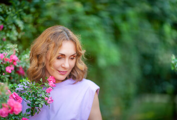 Fototapeta premium Beautiful successful middle aged woman smelling bloom roses and enjoying in garden outdoors.