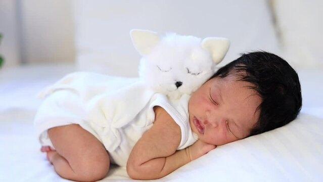 a newborn black African-American baby is sleeping sweetly on his tummy with a soft toy cat, a small dark-skinned baby is lying on the bed in the bedroom in close-up