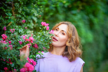 Beautiful successful middle aged woman smelling bloom roses and enjoying in garden outdoors.