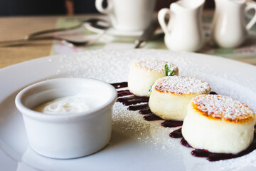 Cottage cheese pancakes with cherry jam and sour cream. Vanilla syrniki on white plate. Sweet curd cheese dessert. Sweet breakfast concept. Curd cheese dessert decorated with jam in cafe. 