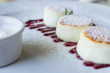 Cottage cheese pancakes with cherry jam and sour cream. Vanilla syrniki on white plate. Sweet curd cheese dessert. Sweet breakfast concept. Curd cheese dessert decorated with jam in cafe. 
