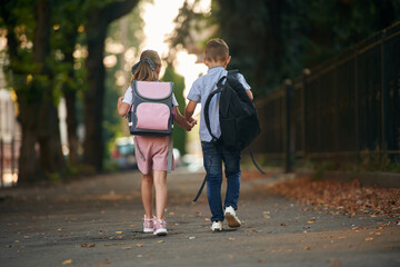 Back view, walking. Young school children of boy and girl are together outdoors