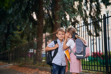 To gossip. Young school children of boy and girl are together outdoors