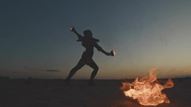 Full length shot of female silhouette dancing with two fire bowls during might fire show