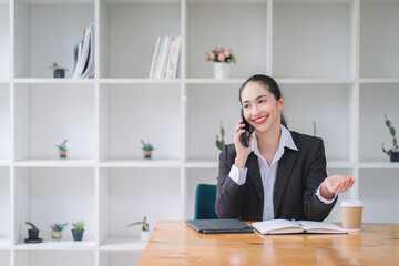 Young adult Asian businesswoman, secretary, sales manager, business consultant, engaging in a phone conversation with a client at the office.