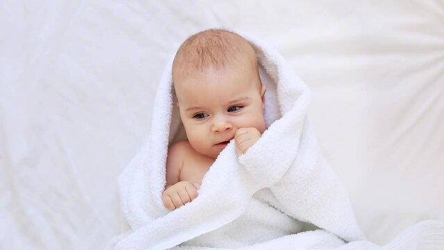 Six month baby wearing towel after bath. Childhood and baby care concept, cute little newborn baby in white towel after bathing