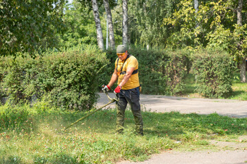 Man gardener mowing tall grass with electric or petrol lawn trimmer in a park. Man mows grass with a gasoline scythe.