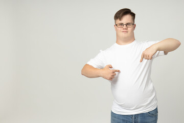 Smiling young man with down syndrome in glasses, jeans and white t-shirt posing in front of the camera, space for text