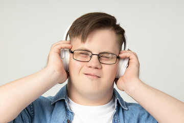 Smiling young man with down syndrome wearing glasses listening to music in headphones